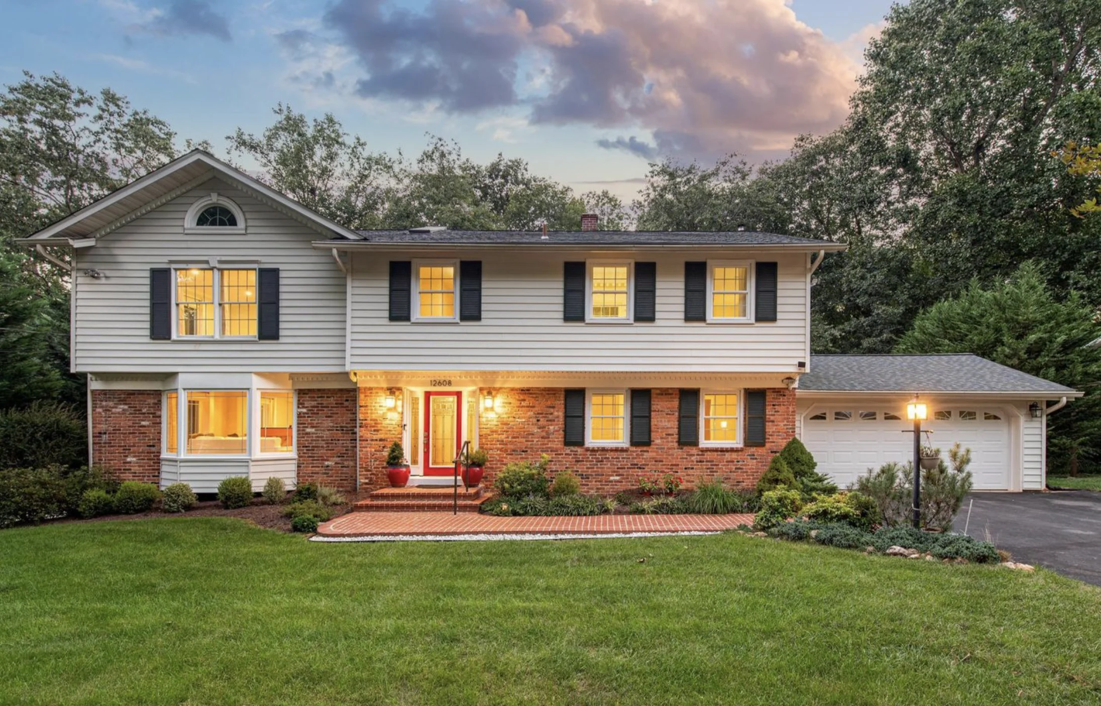 Brick-front home exterior with a red door, brick steps, and landscaped entry